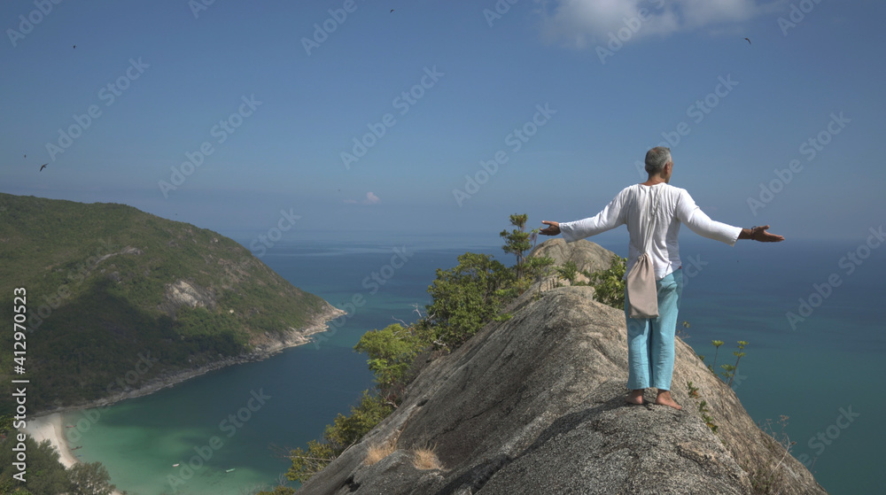 Adult man stands on mountain peak with raised arms against sea view and flying birds Adult man stands on mountain peak with raised arms against sea view and flying birds