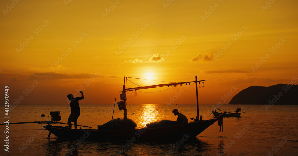 Warm sunset view of fishermans silhouettes in boat