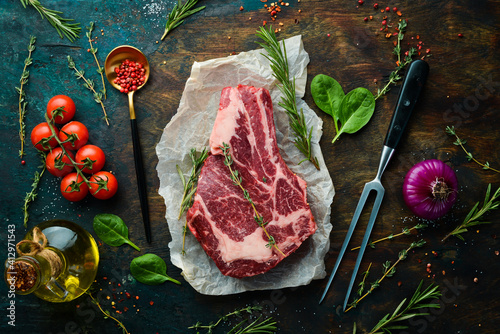 Raw beef ribeye steak on the bone with thyme, rosemary and spices. Top view. Flat lay top view on black stone cutting table. photo