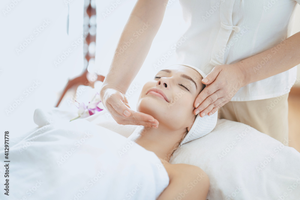 Obraz premium Female massage therapist giving a massage at a spa. Young woman receiving head and facial massage in spa salon.