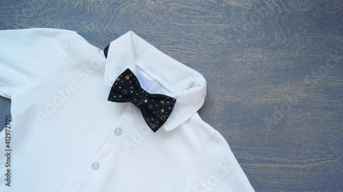 White holiday shirt and black bow tie for boy.Men's outfit on a wooden background.The concept of a holiday, birthday, graduation, knowledge day, men's day