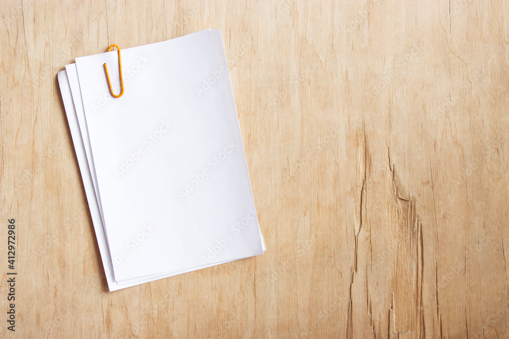 a stack of blank white paper under a paper clip on a wooden table a stack of blank white paper under a paper clip on a wooden table