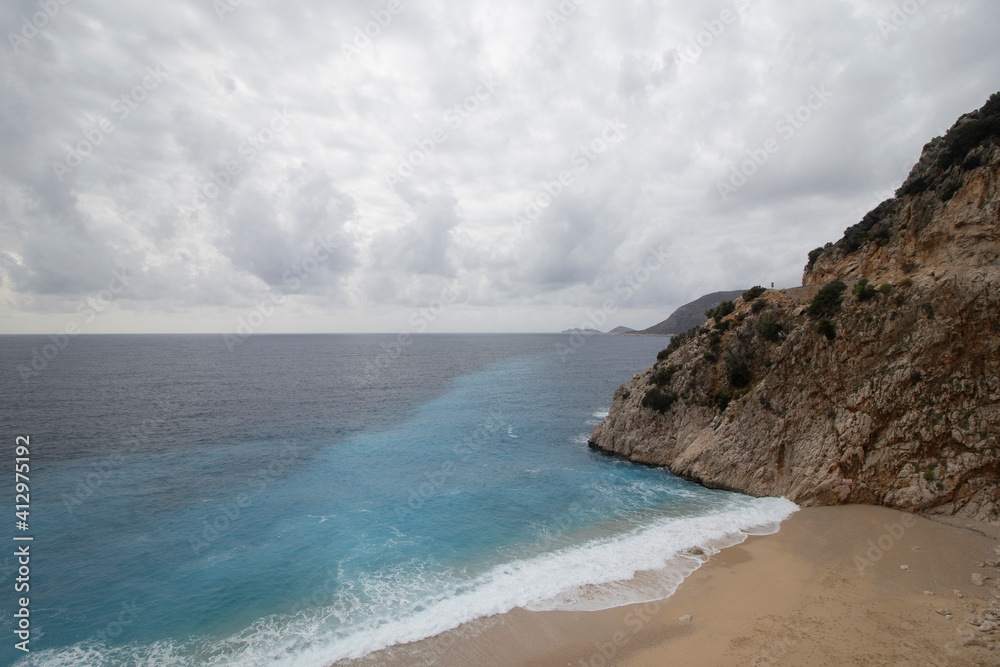 Wide angle seascape with hill,  waves, turquoise sea and  beach 
