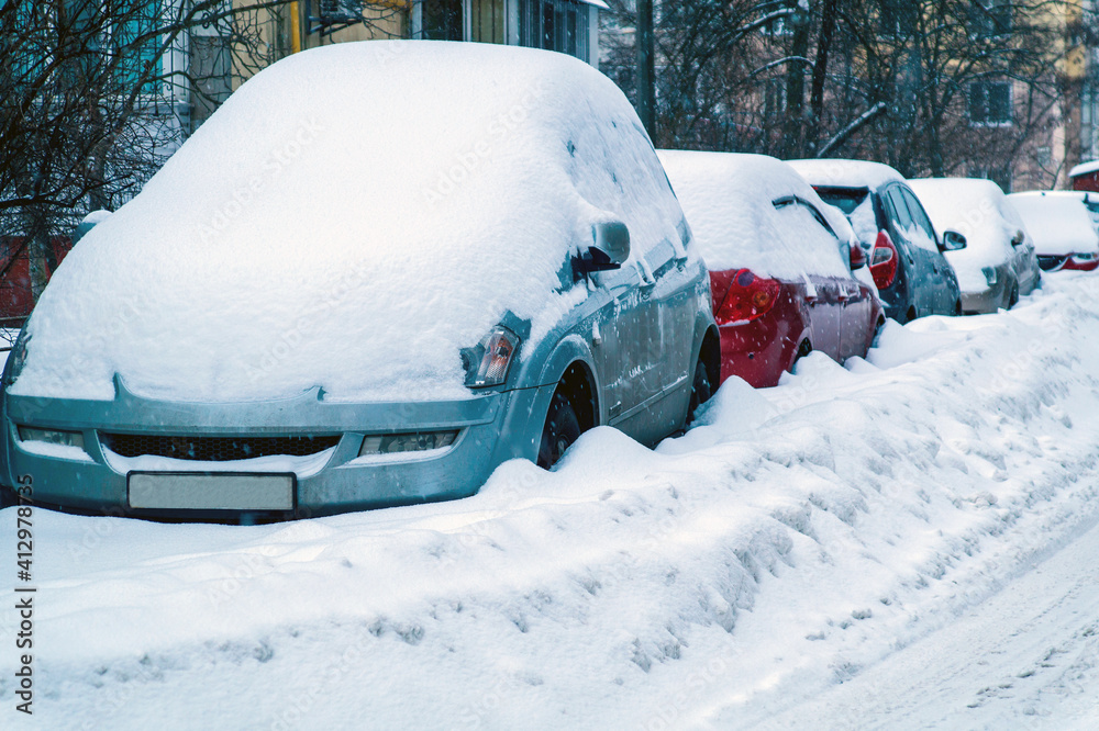 Cars in the parking lot are covered with a thick layer of snow. Concept winter weather and car owner confrontation Cars in the parking lot are covered with a thick layer of snow. Concept winter weather and car owner confrontation