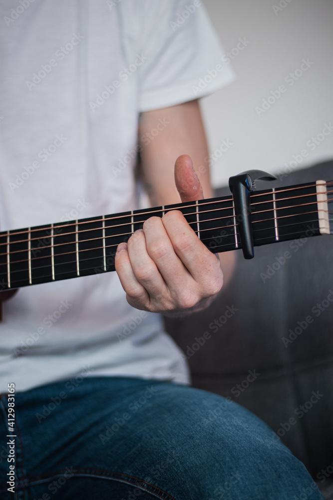 Fototapeta premium part of a wooden guitar and the hand of a singer who changes holding the guitar according to the chord he needs. Special handle for adjusting the tone. Learning new skills during quarantine