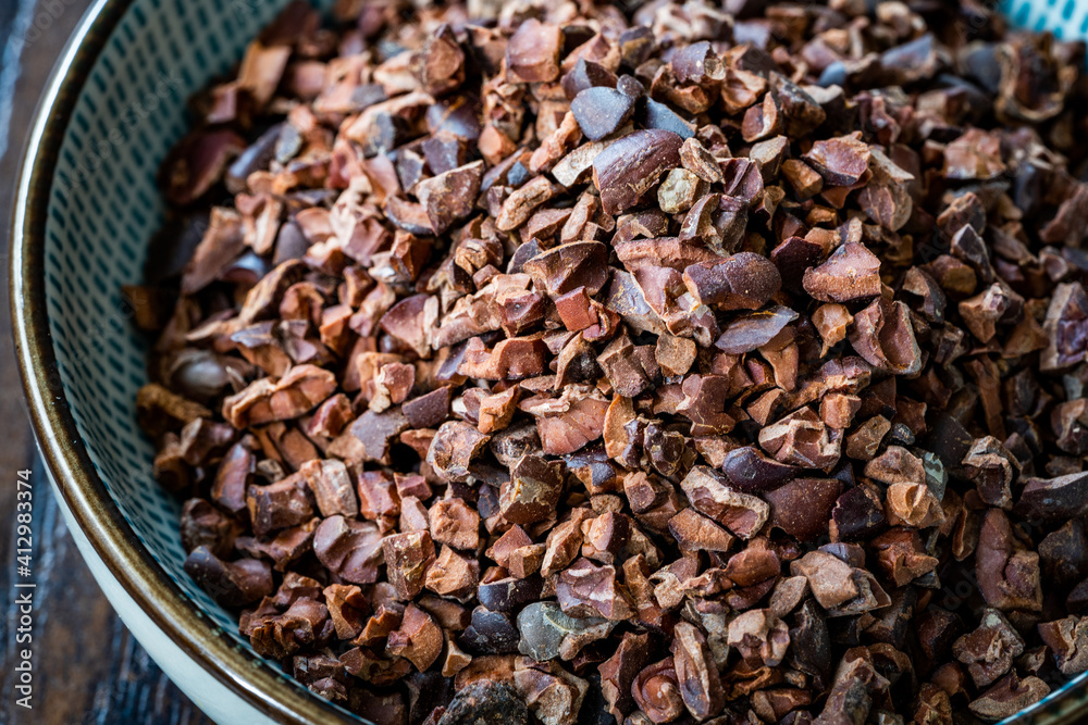 Obraz premium Chocolate Cacao Nibs or Cocoa Nibs in Bowl Ready to Use on Dark Wooden Surface.