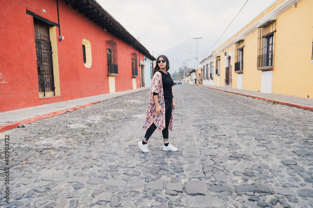 Full portrait of Hispanic woman walking in colonial city on a cloudy day - tourist crossing the street in Antigua Guatemala