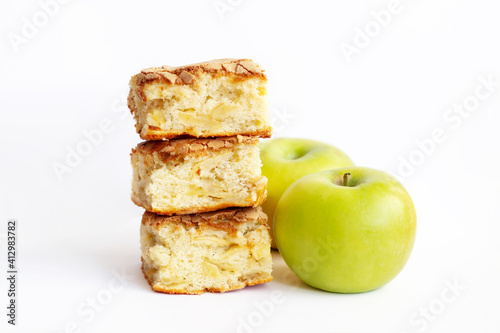 Pieces of homemade organic sponge apple pie near green apples isolated on a white background. Close up of a Dessert Charlotte