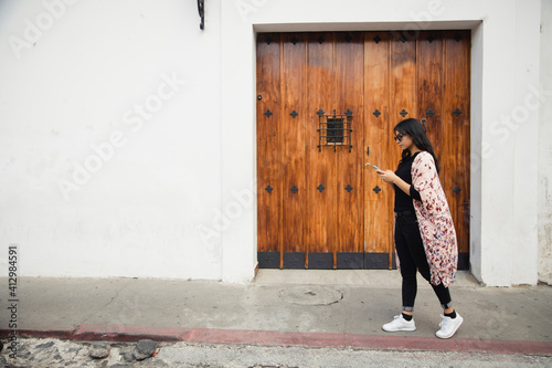 Full portrait of Hispanic woman walking with her phone in colonial city-tourist sending a text message while she walks in Antigua Guatemala