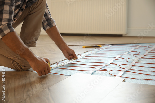 Professional worker installing electric underfloor heating system indoors, closeup photo