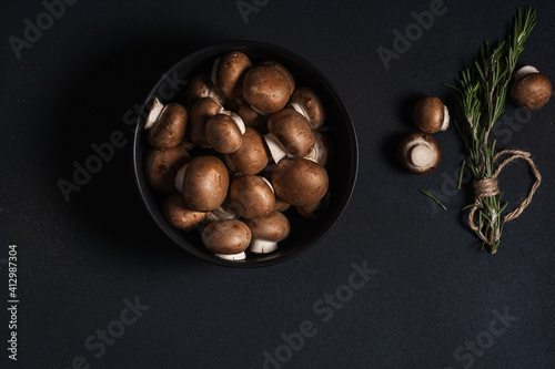Bowl of raw mushrooms and bunch of fresh rosemary, top view