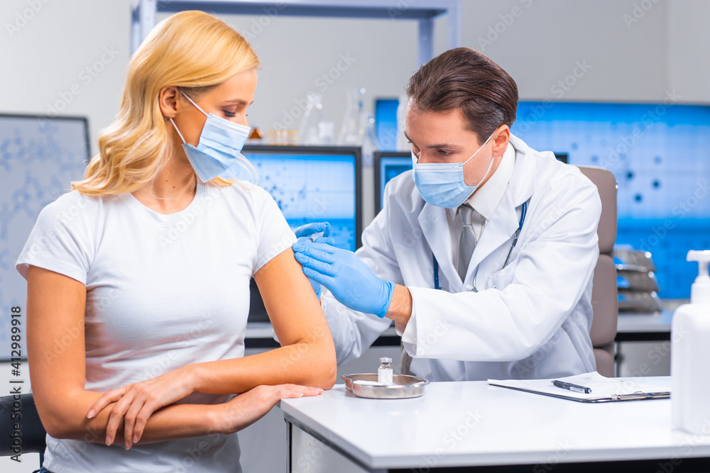 Fototapeta premium Professional doctor makes a coronavirus vaccine using a syringe and hypodermic needle. Professional medical worker and patient at the hospital office. Vaccination and safety.