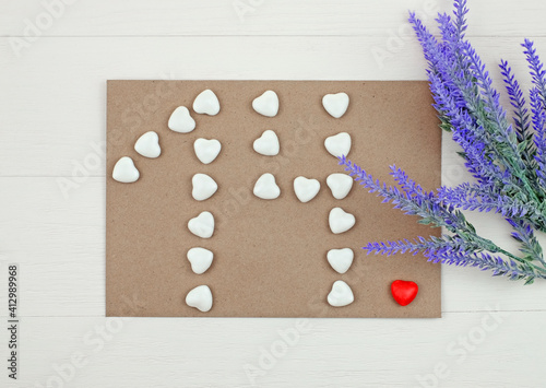 Number 14 formed with hearts candies on envelope and flowers. Top view photo
