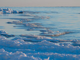 Cold winter sea shore. Pieces of ice by the sea. Blue sky with small clouds
