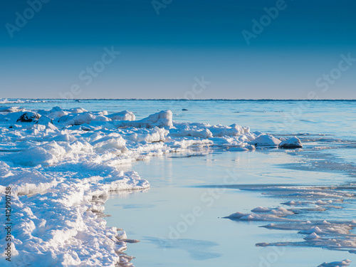Cold winter sea shore. Pieces of ice by the sea. Blue sky with small clouds