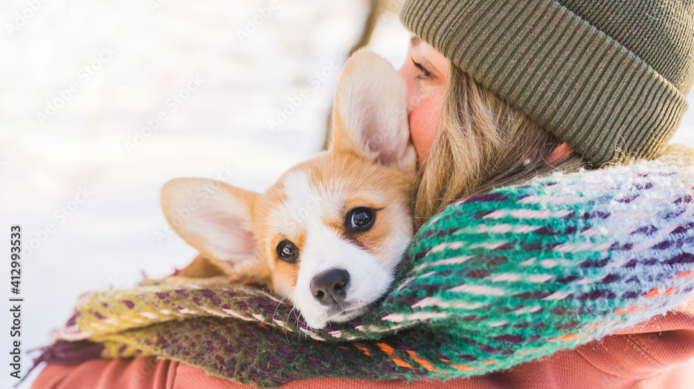 Young happy woman having fun in snowy winter park with Corgi baby dog