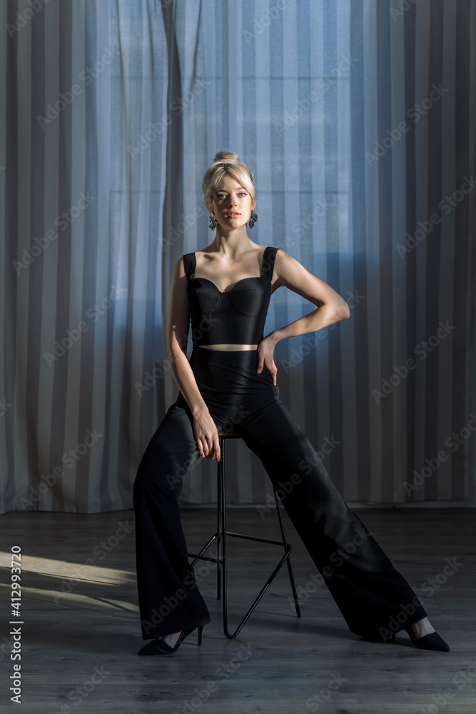Fototapeta premium Studio portrait of a pretty blonde woman in black top and black pants, looking to the camera.