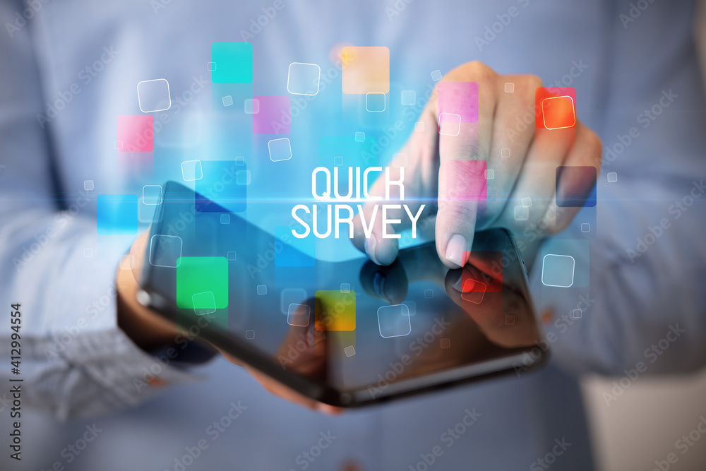 Young man holding a foldable smartphone with QUICK SURVEY inscription, educational concept Young man holding a foldable smartphone with QUICK SURVEY inscription, educational concept