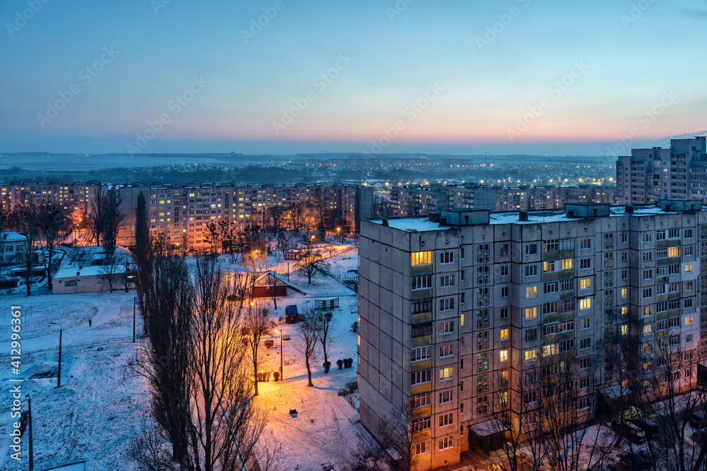 Obraz premium Top view of the evening city in winter with illuminated streets and light in the windows of apartments