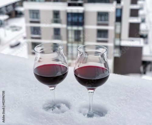Two glasses of red wine on the snow-covered windowsill of the upper floor of the apartment building.