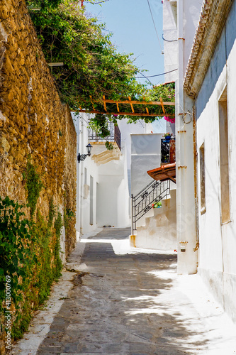 Fototapeta Naklejka Na Ścianę i Meble -  One of the charms of the Greek Cycladic Islands, in the heart of the Aegean Sea are the narrow streets: white houses, small flowered balconies and cobbled stairs