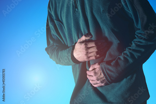 Man holds his belly in pain with both hands against a blue background.