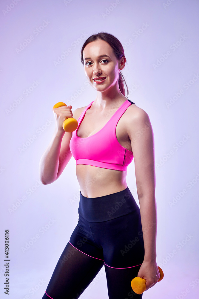 Young beautiful sports girl in leggings and a top does exercises with dumbbells. Healthy lifestyle. A woman goes in for sports at home Young beautiful sports girl in leggings and a top does exercises with dumbbells. Healthy lifestyle. A woman goes in for sports at home