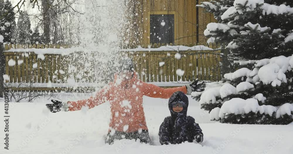 Young woman throwing snow in the air while playing with her kid son near home in deep snow.