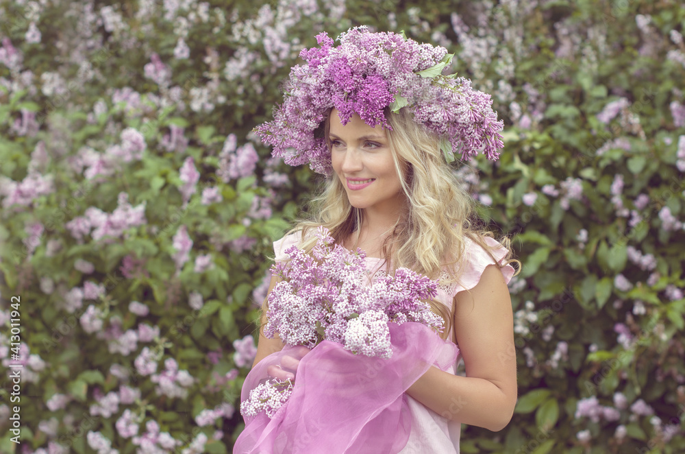 Blonde woman enjoying in a spring garden with blooming lilacs with bouquet, lilac flowers hair style. Spring Concept, Spring blossom, Positive human emotions and feelings. Blonde woman enjoying in a spring garden with blooming lilacs with bouquet, lilac flowers hair style. Spring Concept, Spring blossom, Positive human emotions and feelings.