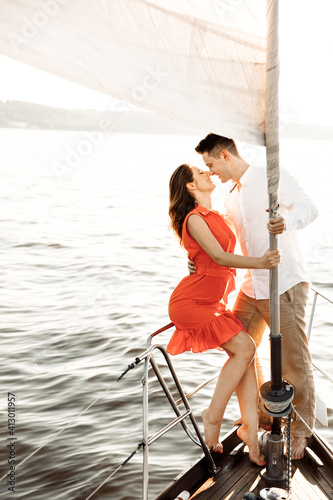 Couple in love holding on to a white sail and kissing on a yacht in the blue sea