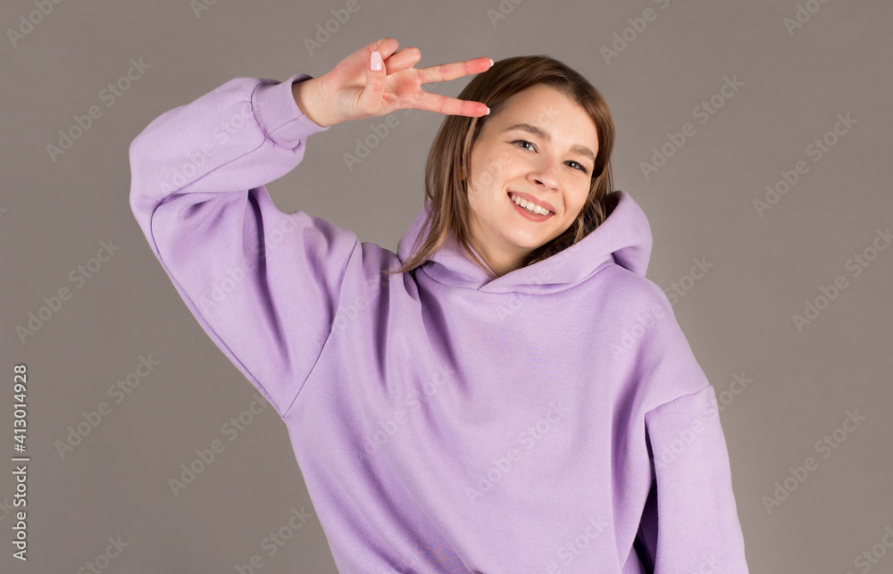 Portrait of cheerful young woman showing two fingers or victory gesture, over grey background Portrait of cheerful young woman showing two fingers or victory gesture, over grey background