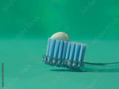 Toothbrush with the recommended amount of toothpaste equivalent to the size of a pea illuminated on a green background