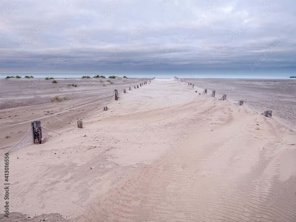 Wooden stakes in light colored sand leading the path towards the sea