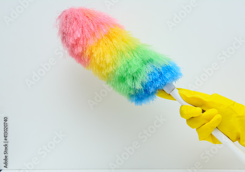 A woman's hand in a yellow rubber glove. There's a feather duster in this hand. White background. Concept-hygiene, maintaining cleanliness