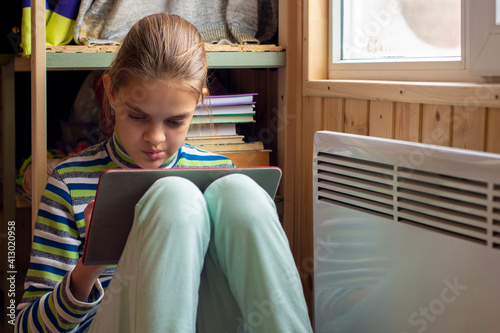 The girl plays in the tablet, sitting in a secluded corner next to the battery