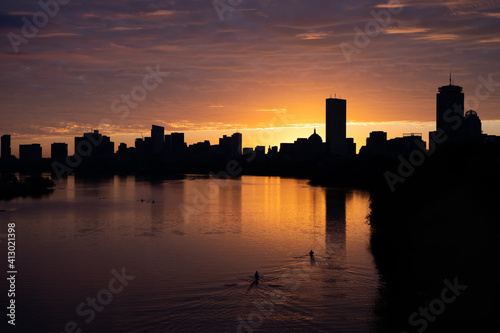 Two rowers on the charles river in Boston during an orange sunrise