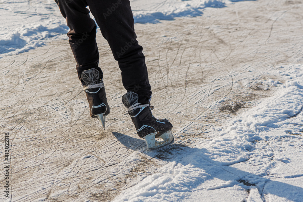 Skater legs at skating rink. Man skating on white ice on frozen lake. Rear view. Winter leisure activity.