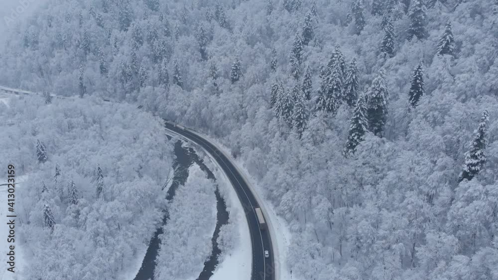 Amazing aerial drone shot: cars and trucks are driving by the road in beautiful winter mountains forest completely covered by white snow. Amazing aerial drone shot: cars and trucks are driving by the road in beautiful winter mountains forest completely covered by white snow.