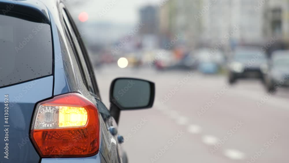 Closeup of rear lamp of a broken car parked on a city street side with blinking signal lights.