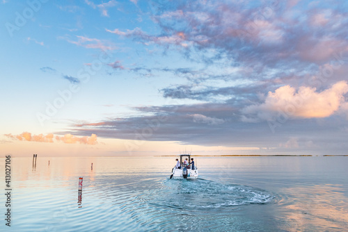 Early morning, a boat heads out on the ocean on a fishing trip in the Florida Keys as the sun rises. The ocean is calm and flat there are a few clouds in the sky. photo