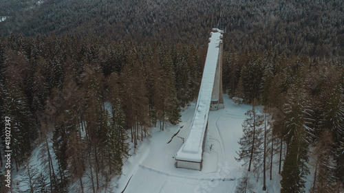 Aerial drone view of old deserted or abandoned famous ski jumping hill in Cortina d'Ampezzo, Italy on a winter day with snow. Visible snowy forest in the background.