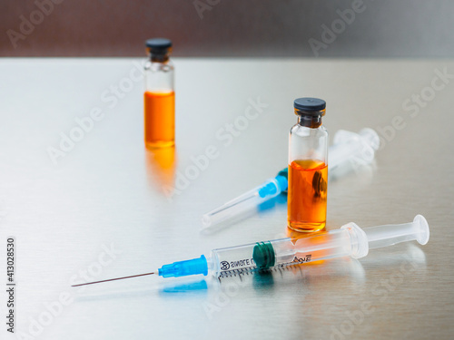 Selective focus. Close-up shot of injection syringes and ampoules with orange coronavirus vaccine on a silver aluminum background. Covid-19 pandemic medical concept. Copy space.