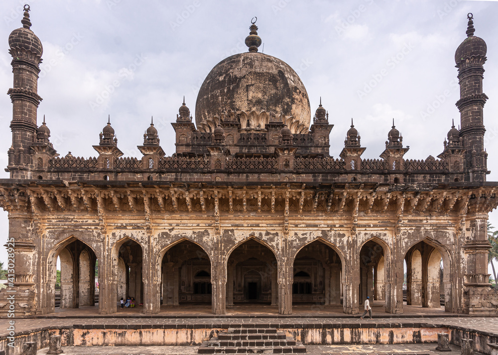 Vijayapura, Karnataka, India - November 8, 2013: West side of brown stone Ibrahim Rauza mausoleum fills entire frame under blue cloudscape.