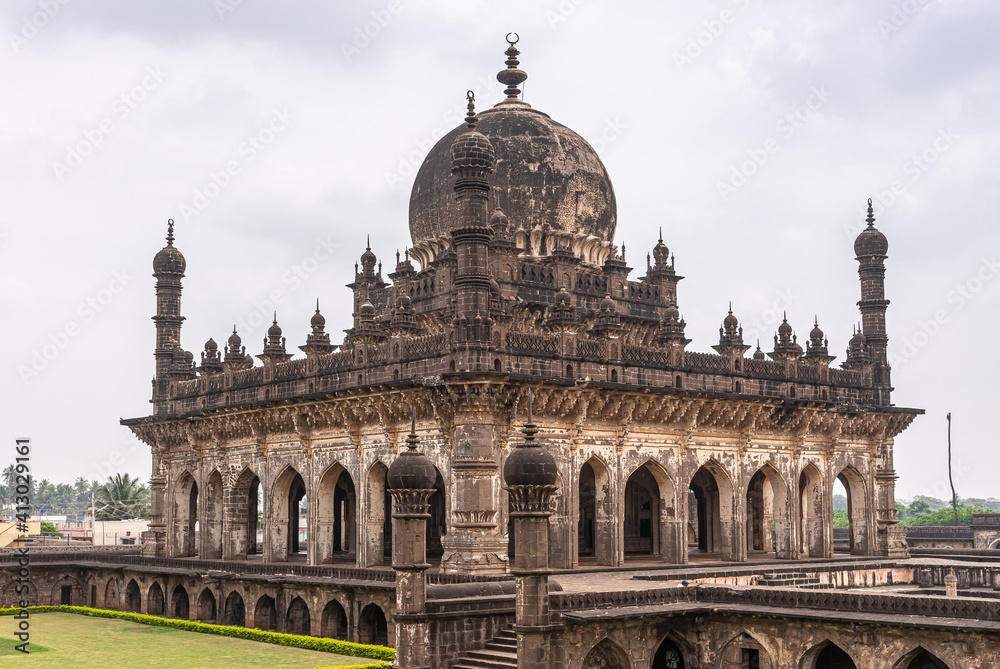 Vijayapura, Karnataka, India - November 8, 2013: NW corner view on brown stone Ibrahim Rauza mausoluem under gray cloudscape. Some green lawns.