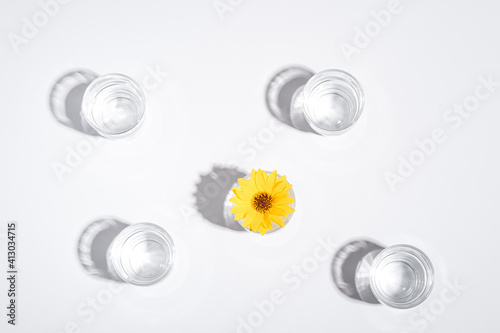 Fresh clear water drink with yellow flower in glass on white background, hard light creative composition, top view
