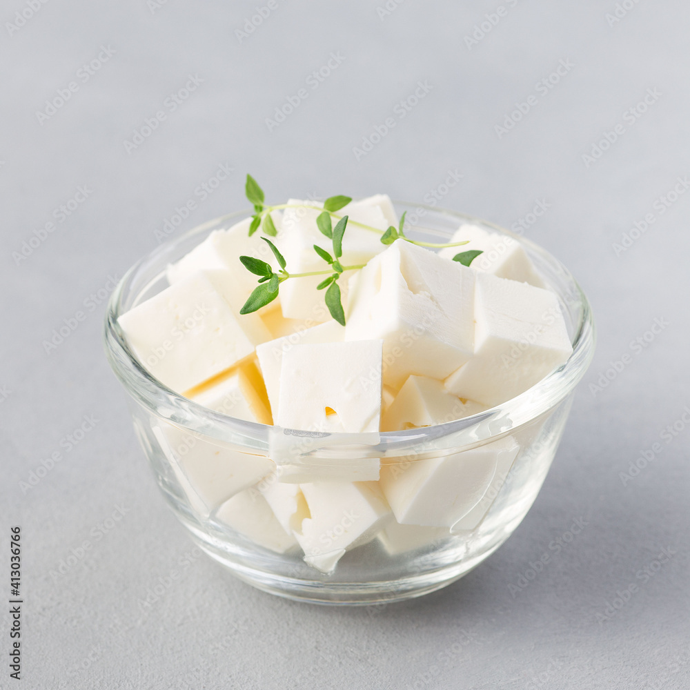 Diced feta cheese garnished with thyme in glass bowl on gray background, square Diced feta cheese garnished with thyme in glass bowl on gray background, square
