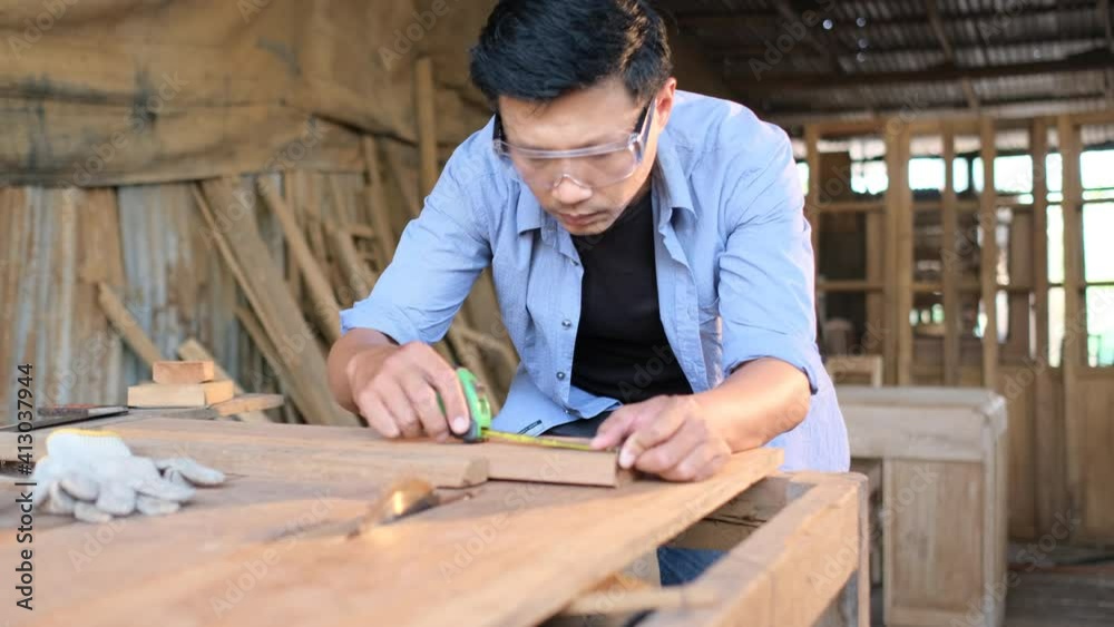 Asian carpenter or craftsman measure length of wood timber and co-worker woman work behind in workplace area. Asian carpenter or craftsman measure length of wood timber and co-worker woman work behind in workplace area.