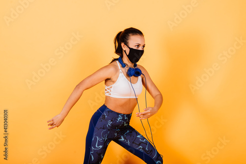 Portrait of fit african woman wearing face mask. Sporty woman in fitness wear standing on yellow background.