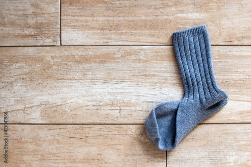 A single ribbed mid-calf blue wool sock that is missing its partner lies on a gold-beige tile floor bathed in sunlight in Toronto, Ontario, Canada, February 2021.