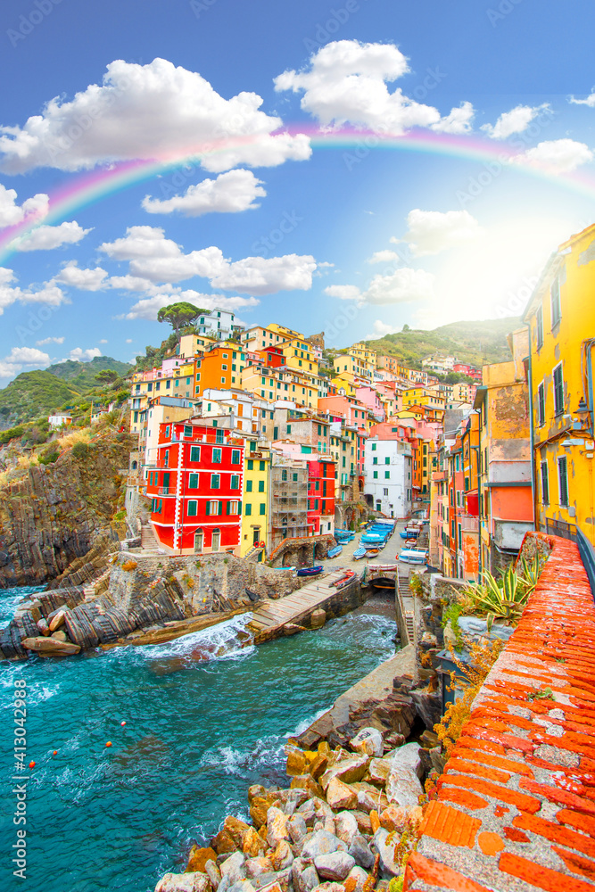 Rainbow on Riomaggiore on the mountain in cinque terre near mediterranean sea in Liguria - Italy and sunny cloudy sky with rainbow, traditional italian architecture